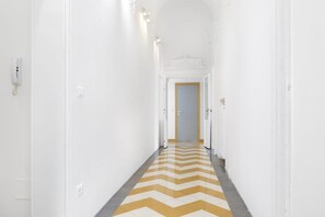Un pasillo estrecho y blanco con piso de diseño en zig-zag, que conduce a una puerta al final.