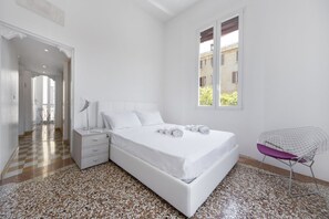 Un dormitorio con una cama grande, una mesita de noche, una silla y una ventana.