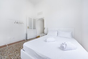 A hotel room with a neatly made bed, a white door, and a tiled floor.