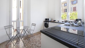 A compact kitchen with a sink, microwave, and a small dining area with a chair and table. - UR-NEST Battisti 2 Deluxe (Bologna)