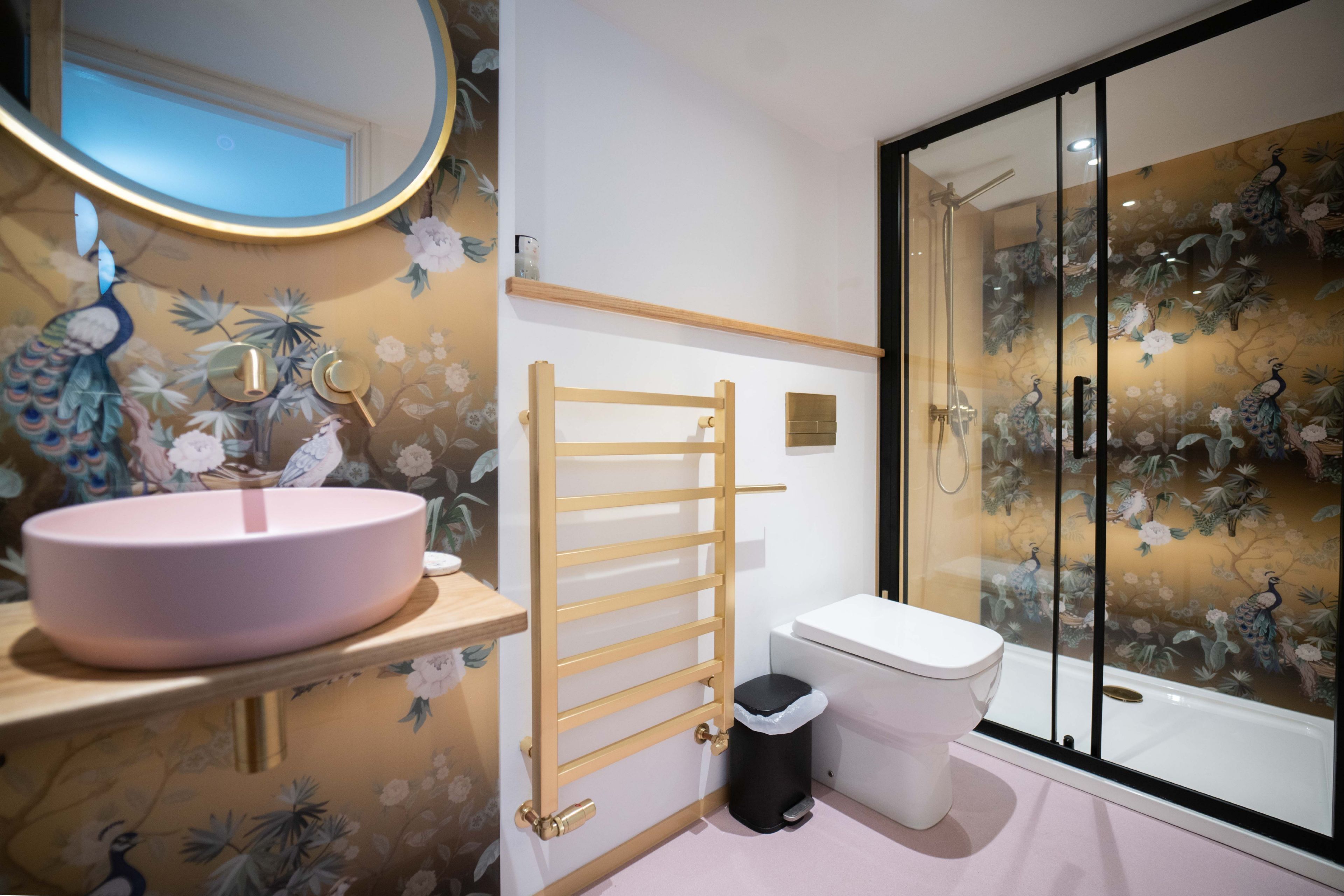 Un baño con lavamanos rosa, inodoro, ducha con puerta de cristal y toallero de madera.