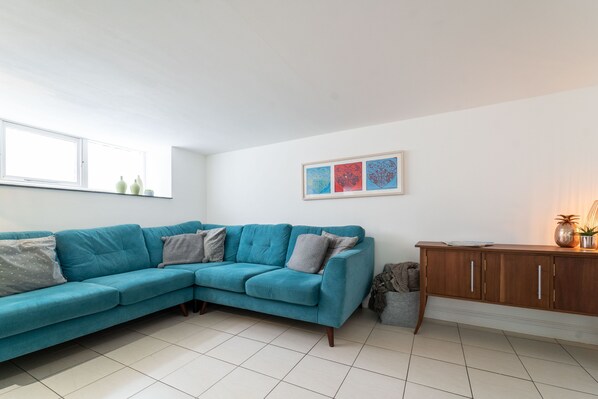 A living room with a teal sectional sofa, a wooden cabinet, and a window with a view.