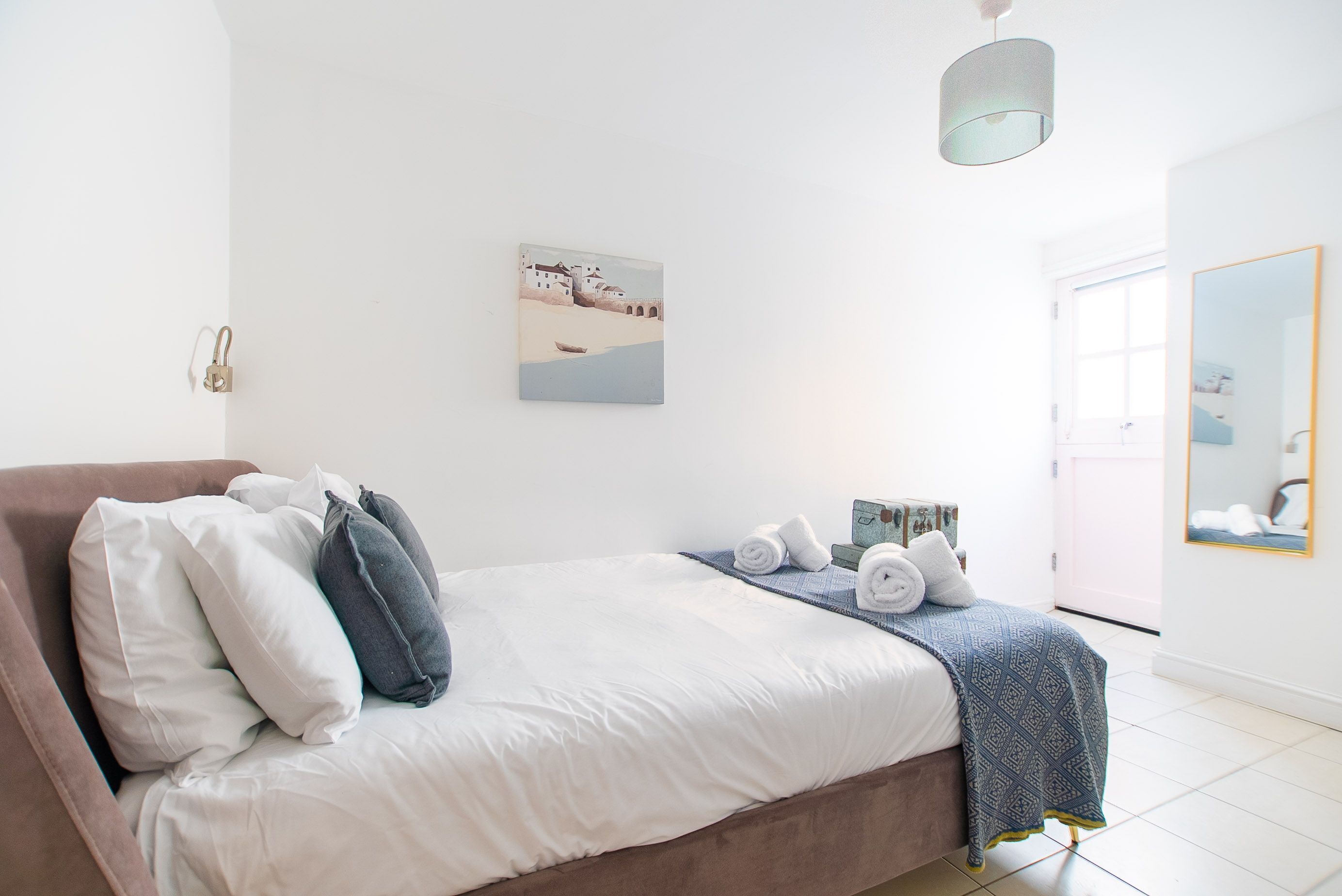 A bedroom with a bed, pillows, a blanket, a painting, a lamp, and a door.