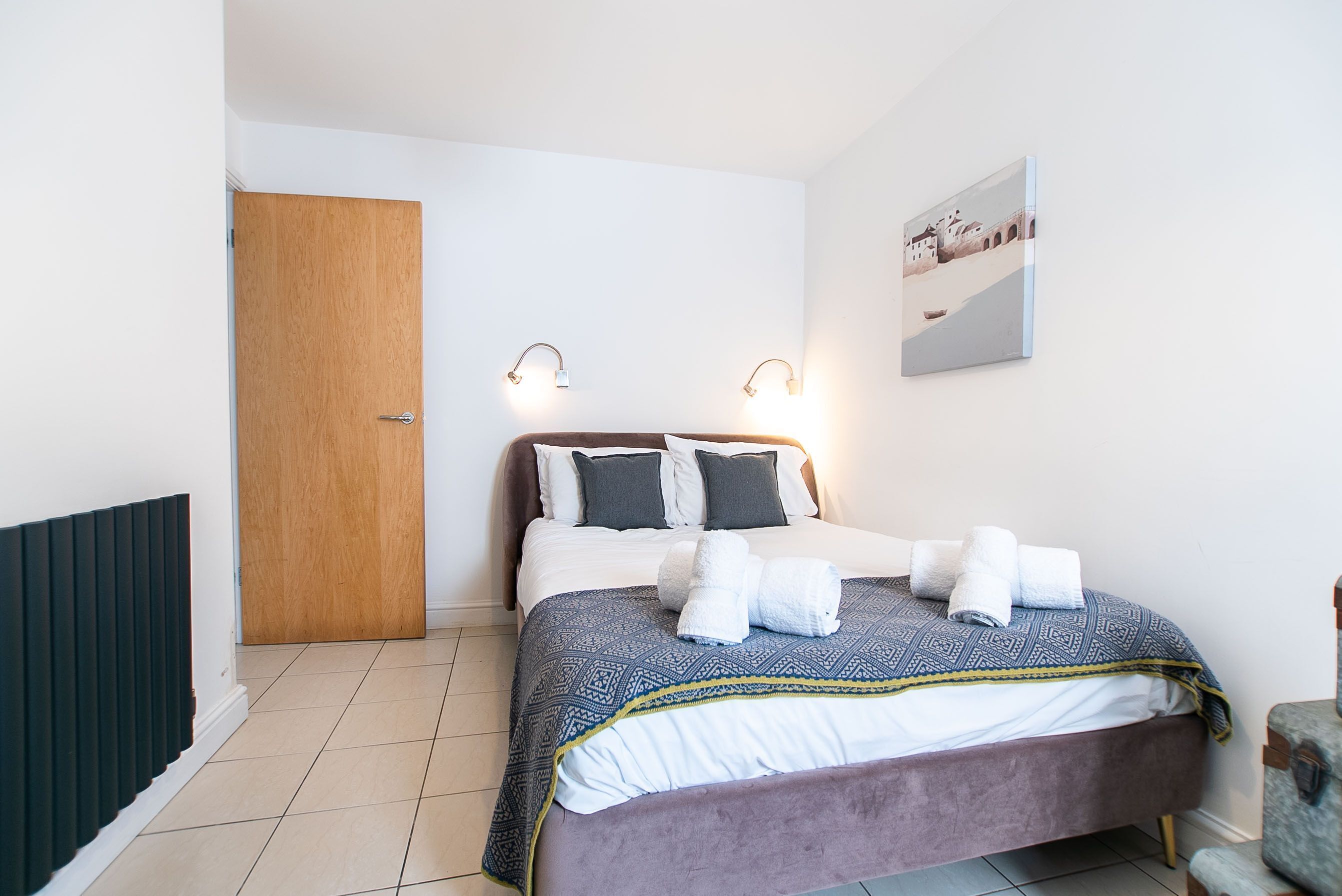 A bedroom with a bed, a wooden door, a radiator, and a wall-mounted picture.
