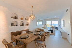 A spacious living area with a dining table set for four, a sofa, and a large window offering a view.