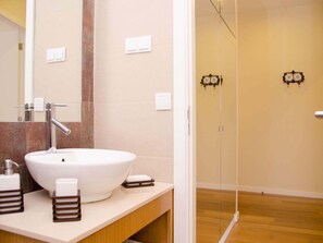 A bathroom with a large white sink, a mirror, and a shower area.