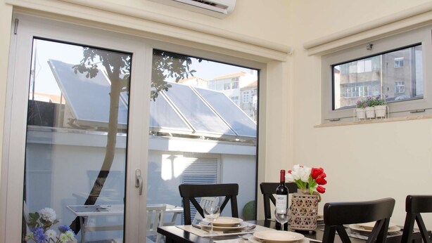 A dining area with a table set for two, a window with a view of buildings, and a solar panel on the roof. - Porto Histórico 4 - Superior one bedroom apartment (Porto)