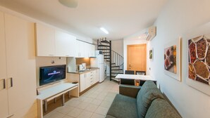 Een kleine leefruimte met een kitchenette, een eethoek, een bank en een trap.