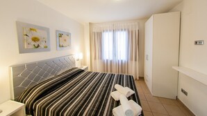 Een hotelkamer met een bed, twee aan de muur hangende schilderijen, een bedlampje, een raam met gordijnen en een kledingkast.