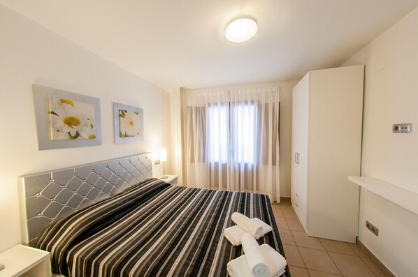 A hotel room with a bed, two wall-mounted paintings, a bedside lamp, a window with curtains, and a wardrobe.