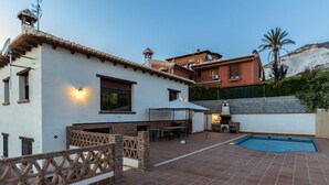 Eine Terrasse mit Swimmingpool, Gartenmöbeln und Grillplatz.
