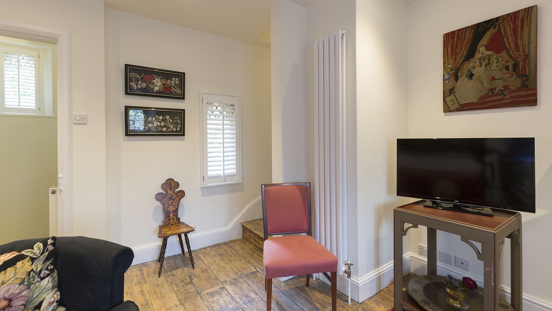 A living room with a television, a red chair, a wooden table, and two framed floral artworks on the wall.