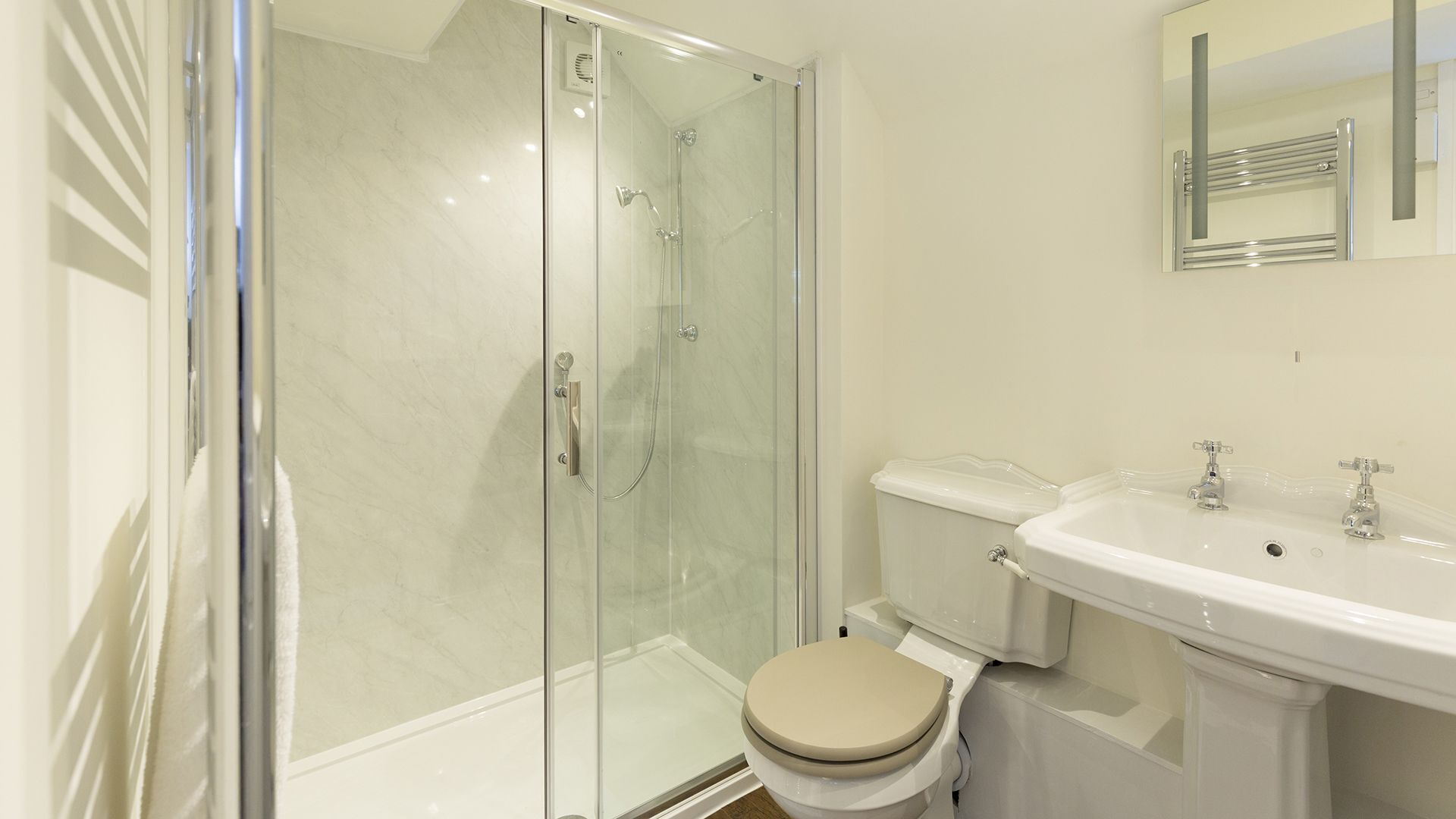 Et moderne badeværelse med en glasafskærmet brusekabine, toilet og et håndvaskspejl.