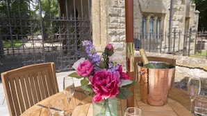 A table with a vase of flowers, a copper bucket, and wine glasses. - Castle Gatehouse -  a sudeley castle cottage that sleeps 4 guests  in 2 bedrooms (Winchcombe)