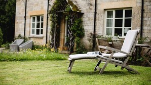 A garden with a lawn, a stone building, and a wooden chair. - A sudeley castle cottage that sleeps 6 guests  in 3 bedrooms (Cheltenham)