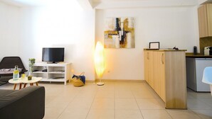 Ein modernes Wohnzimmer mit einer Couch, einem Fernseher, einer Lampe und einer Küchenzeile mit Holzschränken und einem Kühlschrank.