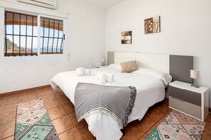 A bedroom with a bed, bedside tables, a nightstand, a window with a view, and a wall with two artworks.