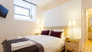 Een slaapkamer met een bed, twee nachtkastjes, een raam en een lamp.