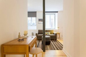 Una sala moderna con un sofá, una mesa de centro y una mesa de comedor con sillas. Hay una ventana con persianas, una lámpara y un cuadro en la pared.