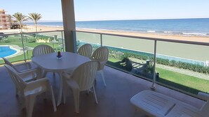 Un balcón con mesa y sillas, con vista a una playa y una piscina.