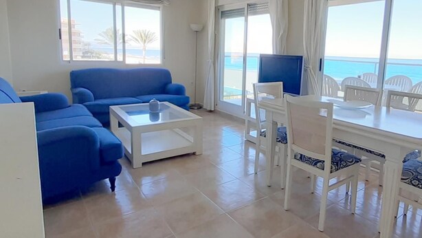 Una sala de estar con un sofá azul, una mesa de centro blanca y un comedor con sillas blancas y una mesa.