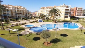 Zona de piscina de hotel con varias piscinas, palmeras y sombrillas.