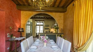 A dining area with a long table set for four, flanked by white chairs. An ornate chandelier hangs from the ceiling, and a yellow curtain is partially visible on the right. - Villa in Montevarchi with 5 bedrooms sleeps 12 (Montevarchi)