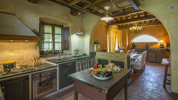 A rustic kitchen with a stone countertop, wooden cabinets, and a dining area with a table set for two. - Villa in Montevarchi with 5 bedrooms sleeps 12 (Montevarchi)