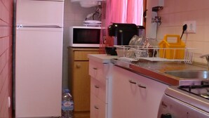 Une cuisine compacte équipée d’un réfrigérateur, d’un four à micro-ondes, d’une cuisinière et de meubles de rangement en bois.