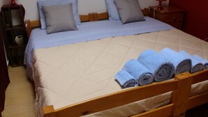 Un lit bien fait, avec une couette beige et deux oreillers, une tête de lit en bois et une table de chevet en bois sur laquelle se trouve une lampe rouge.