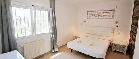 Een slaapkamer met een bed, nachtkastjes, een radiator, een raam met gordijnen en een wandlamp.