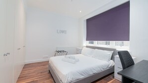 Een moderne slaapkamer met een bed, een bureau en een raam met een paars rolluik.