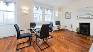 Een moderne woonkamer met een glazen eettafel, zwarte stoelen, een open haard en grote ramen.