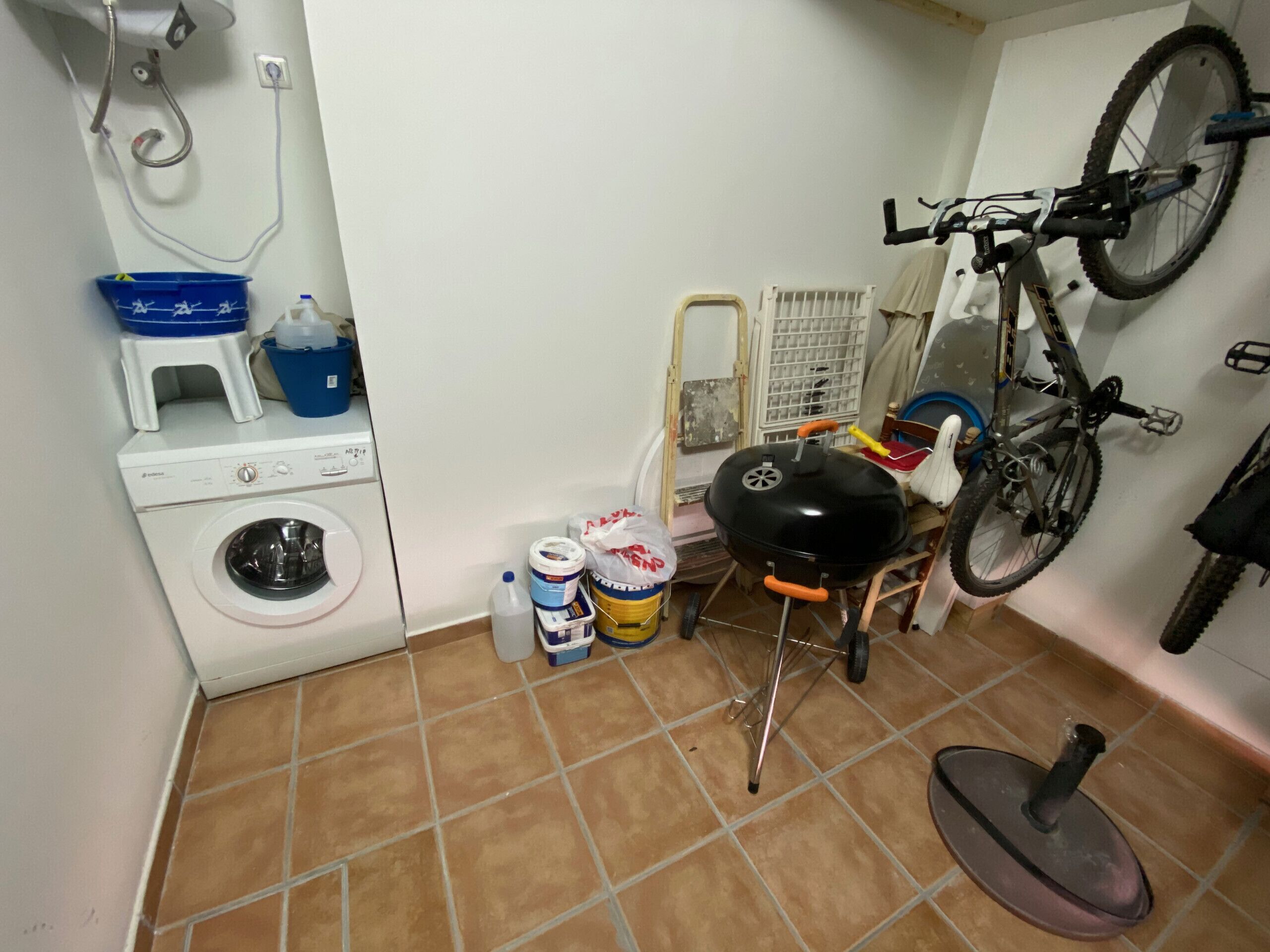 Una cuina compacta amb rentadora, una barbacoa i una bicicleta penjada a la paret.