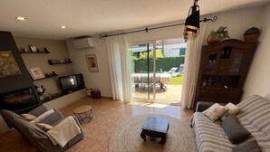Een woonkamer met een bank, een televisie, een open haard, een eethoek en een schuifpui naar een tuin.