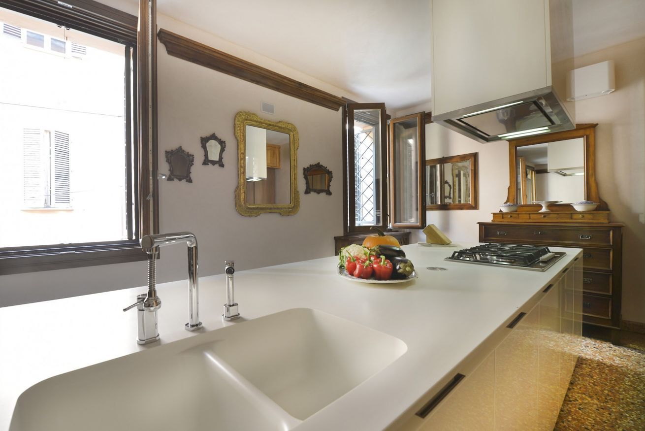 Una cocina con encimera blanca, un lavabo doble, estufa y varios espejos decorativos.