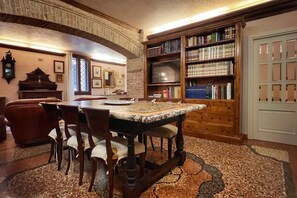 A library with a round table, chairs, bookshelves, and a clock on the wall. - UR-NEST Guerrazzi Deluxe (Bologna)