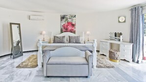 Une chambre à coucher comprenant un lit, des tables de chevet, une coiffeuse et une grande fenêtre avec des rideaux.