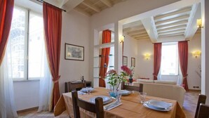 A dining area with a wooden table set for four, red curtains, and a cityscape view through the window.
