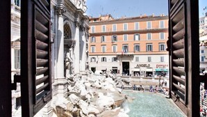 A view of the Trevi Fountain with classical architecture and a busy street in the background.