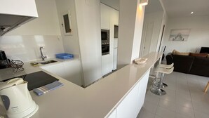 Eine moderne Küche mit weißen Schränken, einem eingebauten Backofen und einer Essecke mit einem Barhocker.