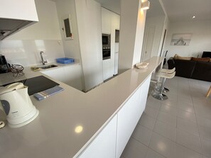 A modern kitchen with white cabinetry, a built-in oven, and a dining area with a bar stool. - Mare Nostrum 3D 541 - Sea views, A/C, renovated (Torroella de Montgri)