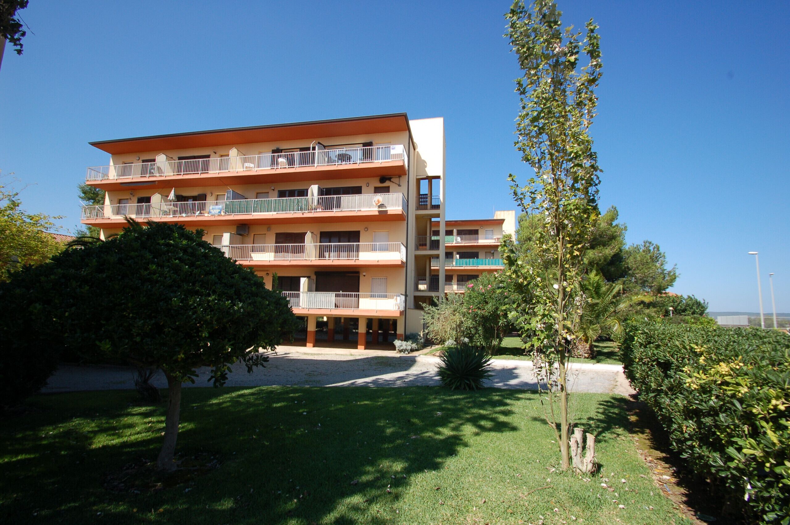 Un edificio residenziale a più piani con balconi, un prato curato e un cielo sereno.