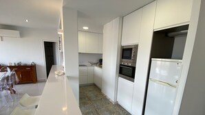 Eine moderne Küche mit weißen Schränken, einem eingebauten Backofen, einer Mikrowelle und einem Kühlschrank. Es gibt einen Essbereich mit einem weißen Tisch und Stühlen.