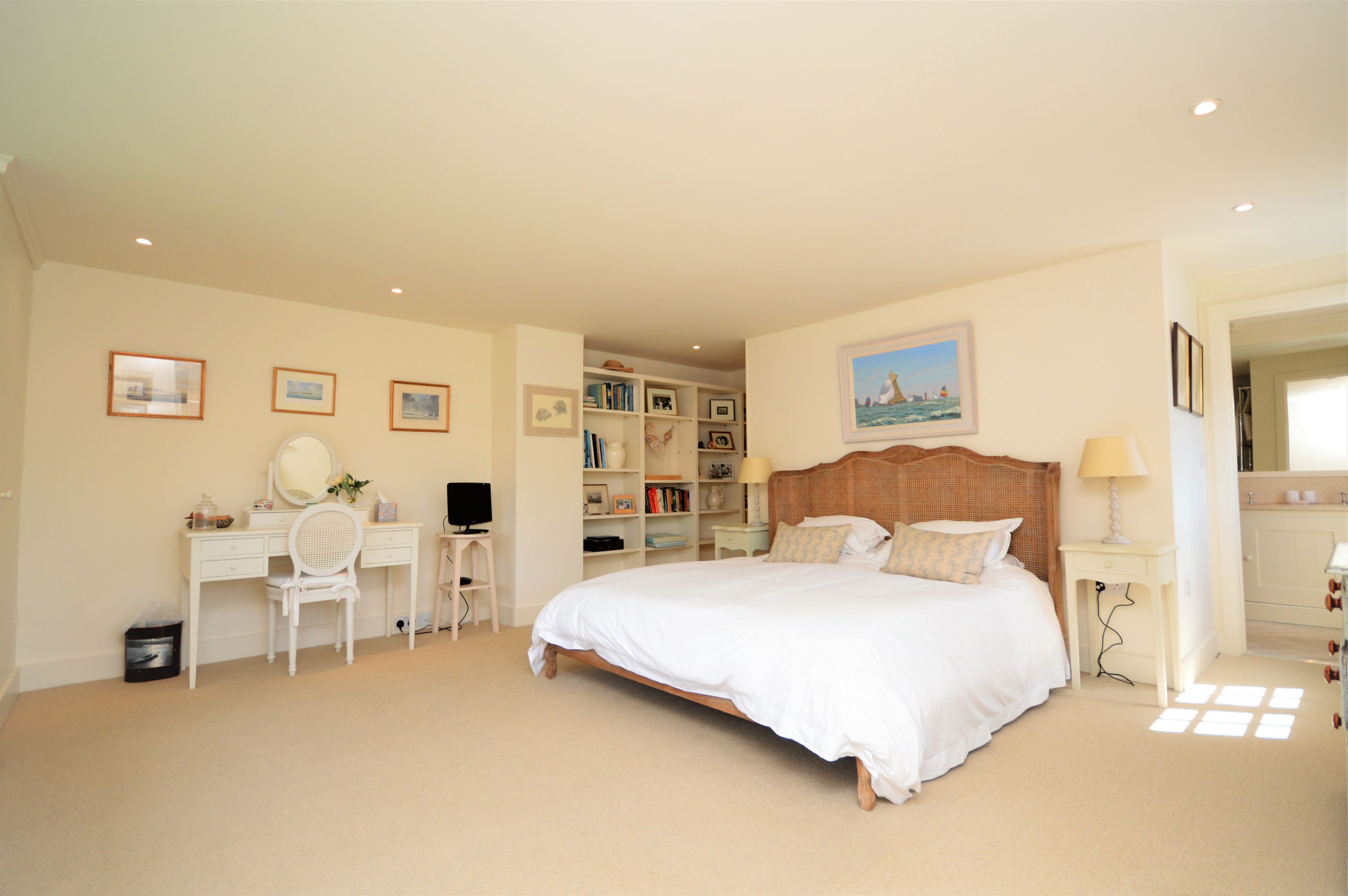 A bedroom with a large bed, a desk, a chair, a bookshelf, and a mirror.