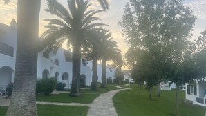 A pathway leading to a building with white walls and arches, surrounded by palm trees and greenery. - 2 Bedroom Apartment , Son Bou (Son Bou)