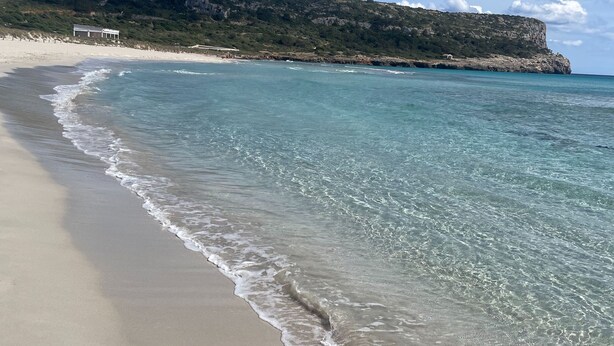 A beach with clear turquoise water, a sandy shore, and a rocky cliff in the background. - 2 Bedroom Apartment , Son Bou (Son Bou)