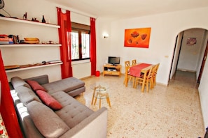 A living room with a sofa, a TV, a dining table with chairs, and a painting on the wall.
