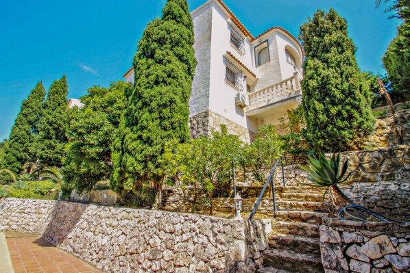 A multi-story building with stone walls and balconies, surrounded by lush greenery and trees.