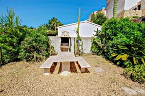 A patio with a barbecue grill, surrounded by cacti and shrubs.